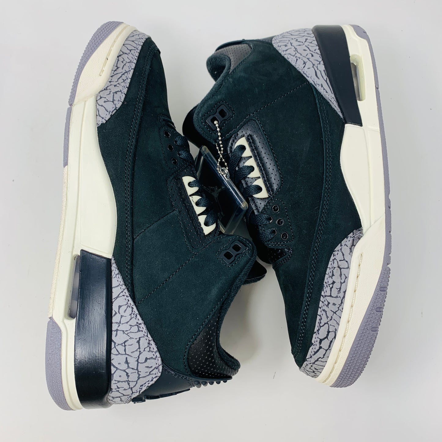 The Jordan 3 Retro Off Noir (W) sneakers from Jordan, featuring a black and gray color scheme with white midsoles and an elephant print design on the heel and toe, are displayed side by side on a white background.