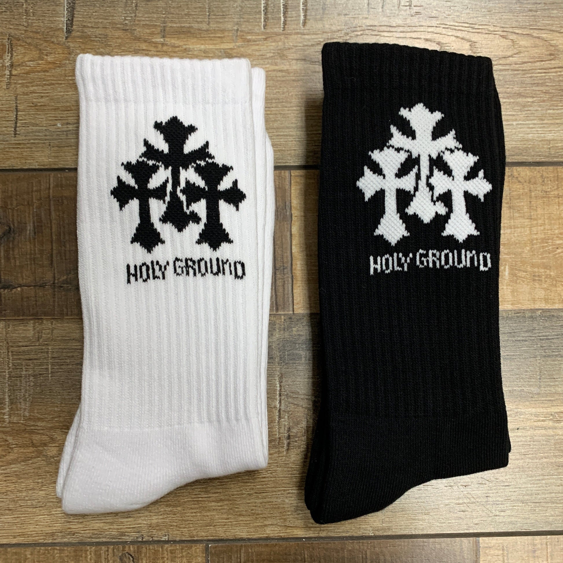 White and black Holy Ground Socks with spiritual design placed on wooden surface.