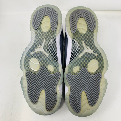 The image displays the soles of a size 9.5 pair of Jordan 11 Retro Low Cool Grey sneakers, featuring a unique tread pattern and visible logo. The slightly yellowed soles have black and grey accents, while the pristine uppers hint at careful maintenance since their 2018 release.