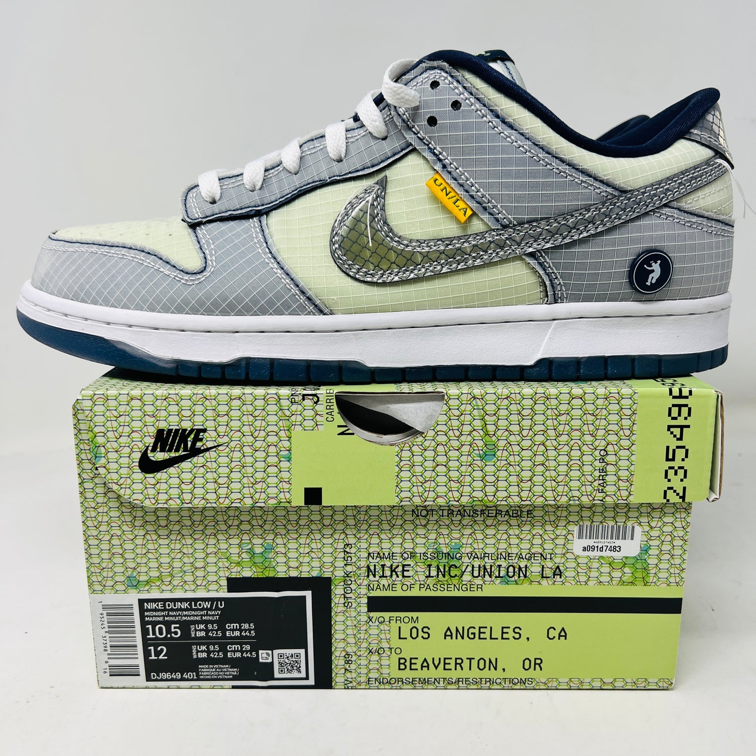 The 2022 Nike Dunk Low Union Passport Pack Pistachio sneaker, with a gray and white grid pattern, silver Swoosh, blue sole, yellow tag, and heel logo sits on the box. Extra laces offer versatility. The box label shows details and size.