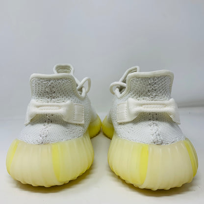 The Yeezy Boost 350 V2 Cream sneakers, from the Yeezy brand, showcase textured white fabric with thick yellow-tinted soles and heel loops, viewed from the back against a simple light background.