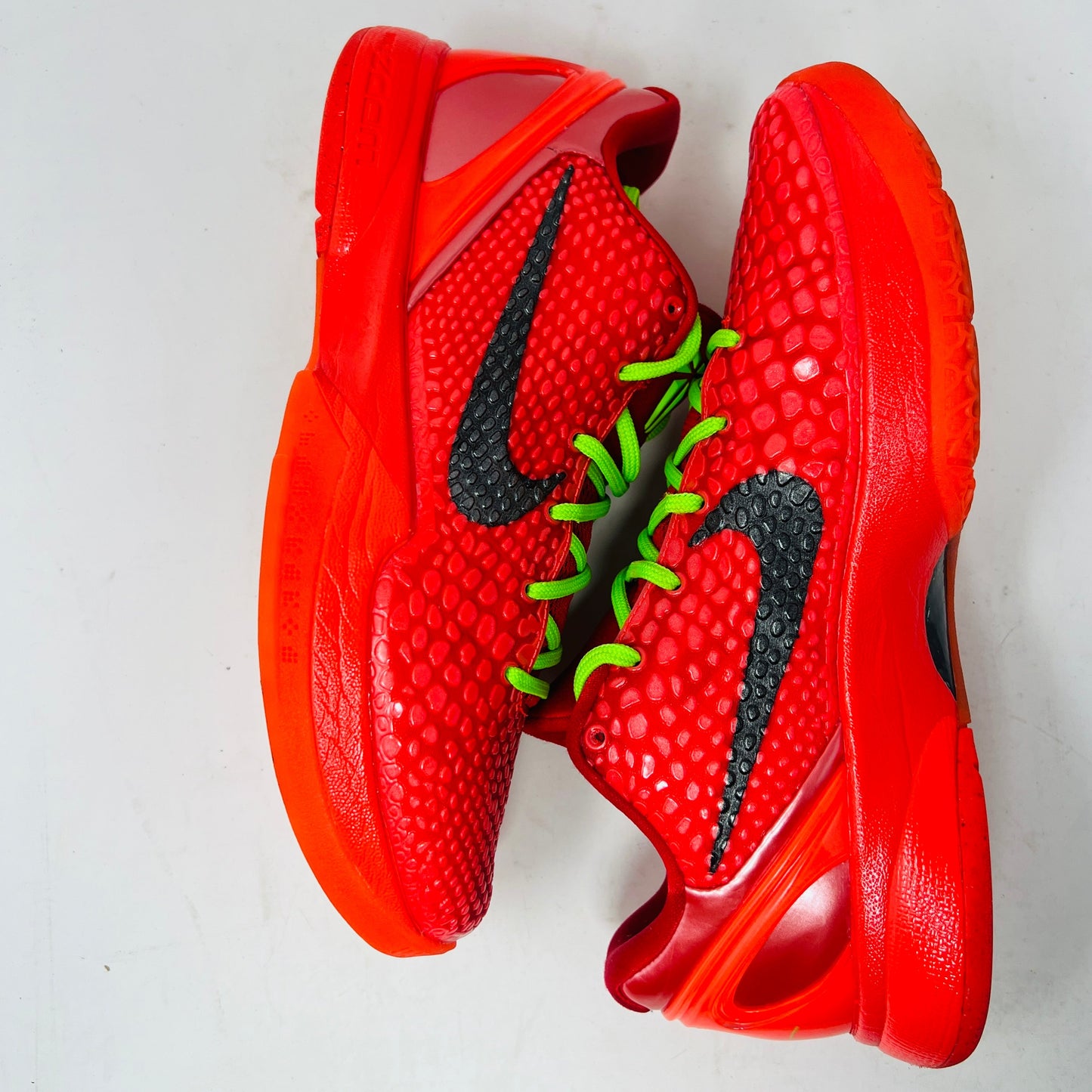 Red Nike Kobe 6 Protro Reverse Grinch sneakers with black swoosh and green laces.