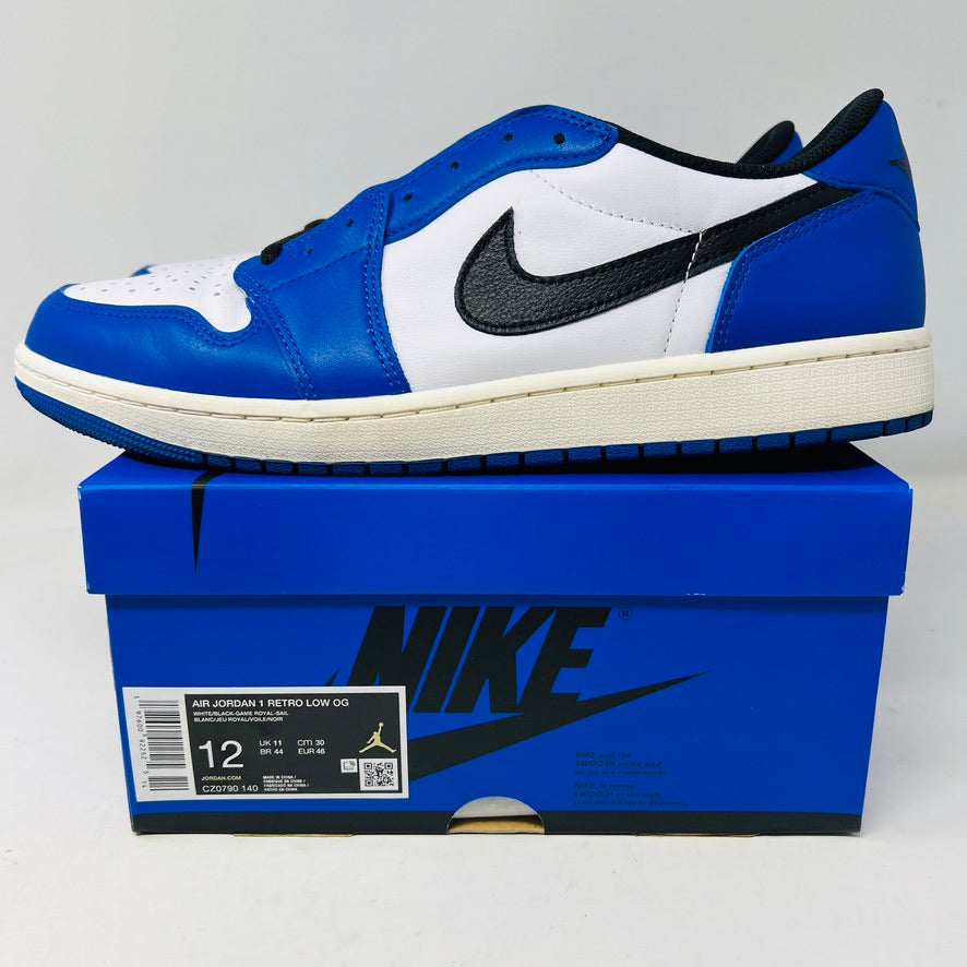 A Jordan 1 Retro Low OG Game Royal shoe in blue, white, and black is showcased on a matching blue Nike box. It features a black swoosh logo and the box label indicates size 12.