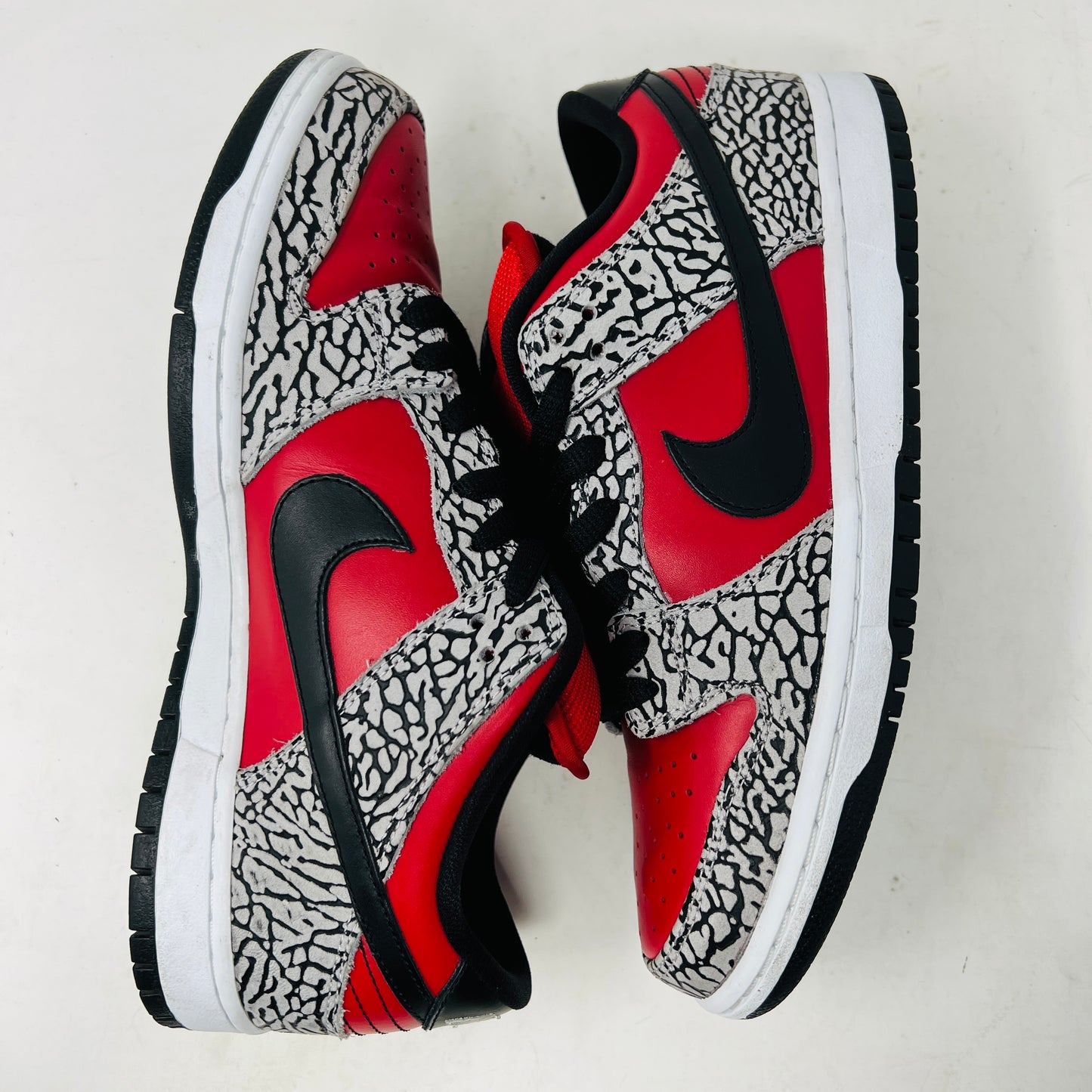 A genuine Nike SB Dunk Low Supreme Red Cement (2012) sneaker, featuring red and black elephant print details, rests on a cardboard box and comes with extra white laces for added style versatility.