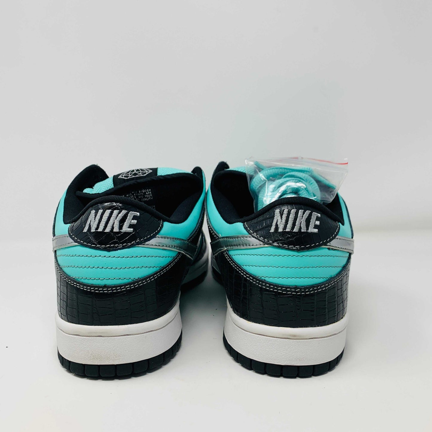 Nike SB Dunk Low Diamond Supply Co sneaker in black and white with turquoise accents, rear view.