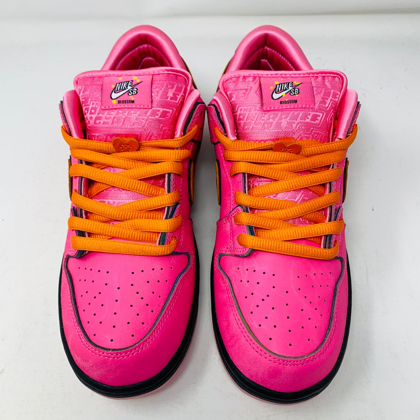 The Nike SB Dunk Low The Powerpuff Girls Blossom sneakers, with their vibrant pink hue and orange laces, capture Blossoms playful spirit. Featuring a low-top design, perforated toe boxes, and the iconic Nike logo on the tongue, they are showcased on a white surface.