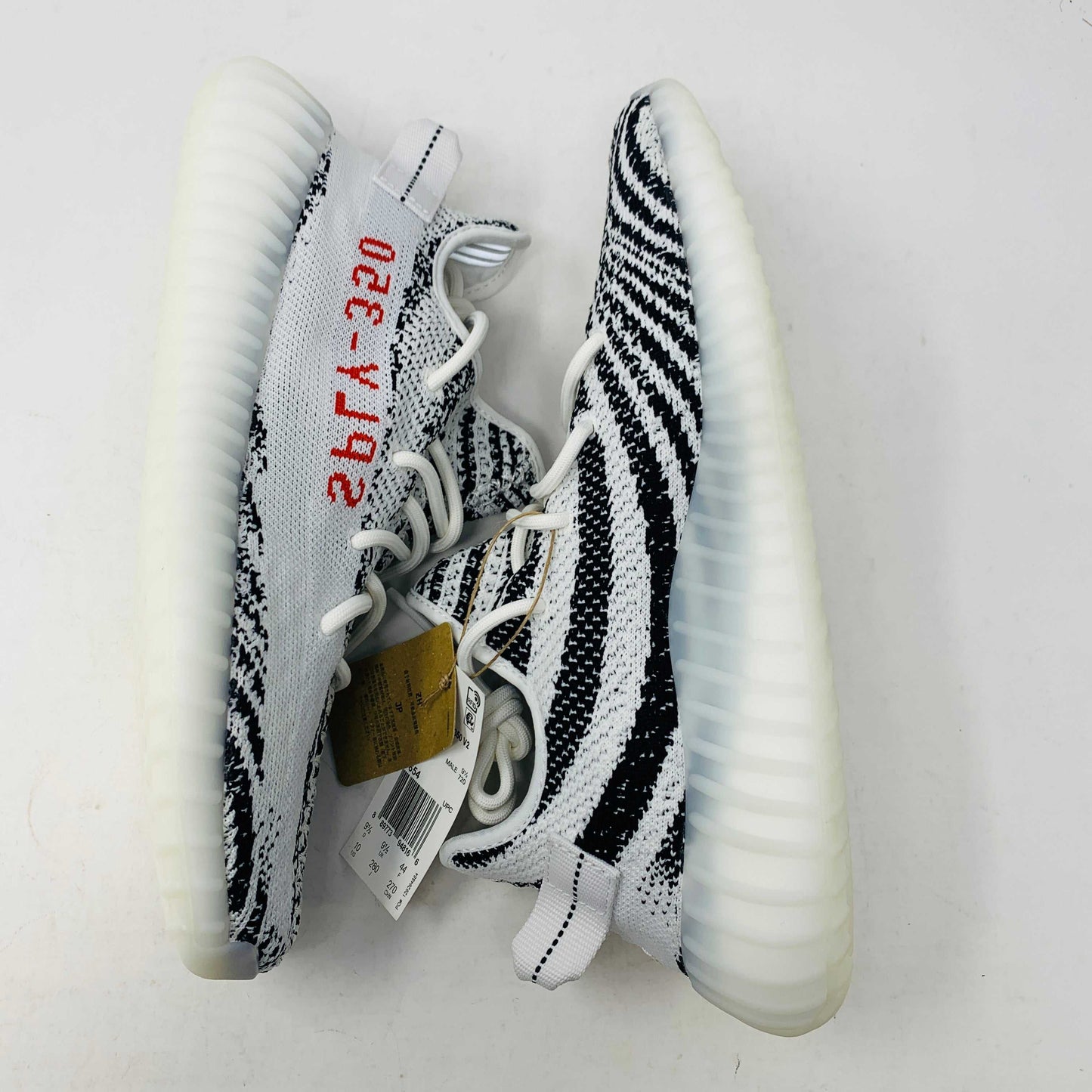 The Yeezy 350 V2 Zebra sneaker, 100% authentic, showcases SPLY-350 in bold red on a white and black design. Packaged in a box marked YZY 350 V2 MADE BY ADIDAS, it features a ribbed sole and knitted upper, effortlessly blending style and comfort.