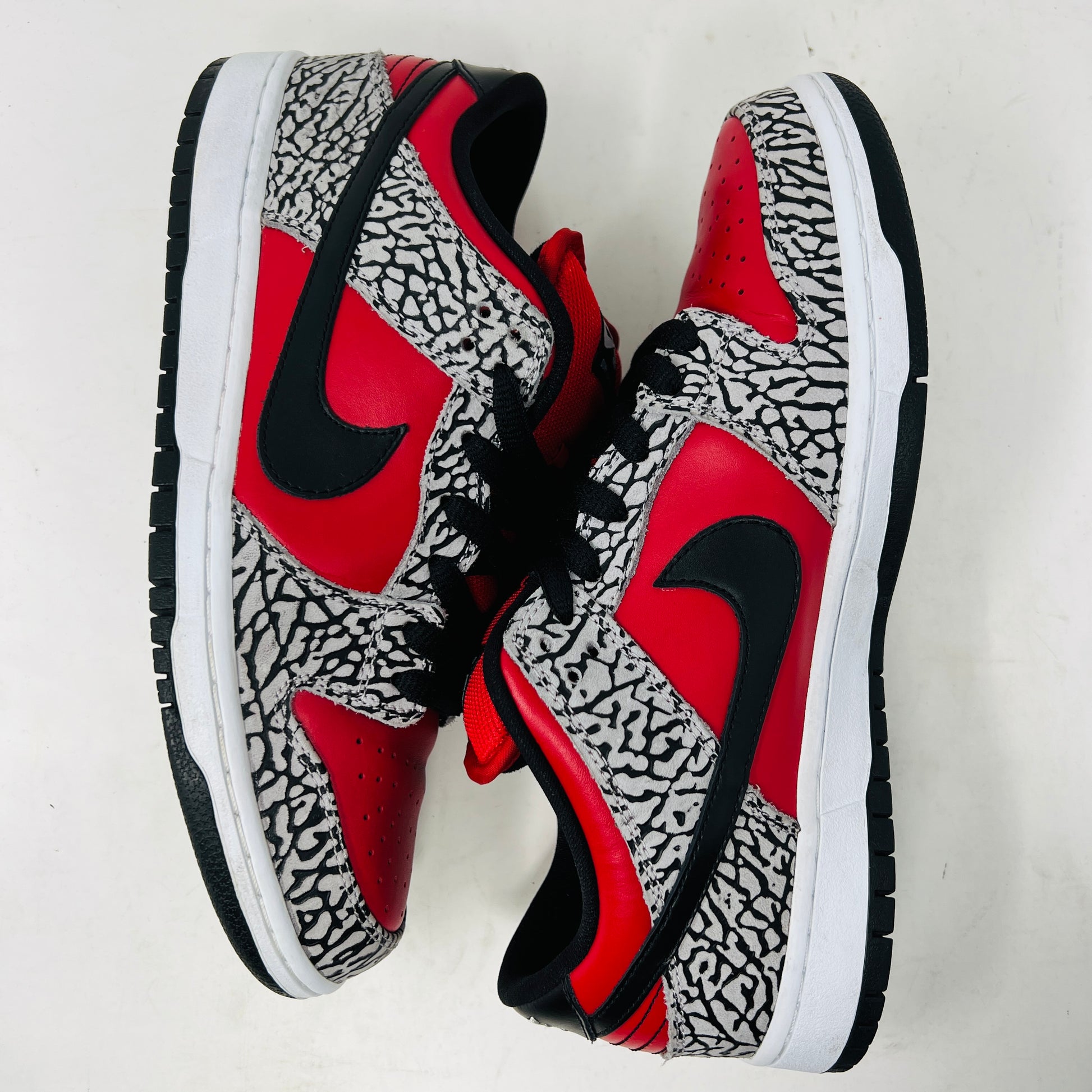 A genuine Nike SB Dunk Low Supreme Red Cement (2012) sneaker, featuring red and black elephant print details, rests on a cardboard box and comes with extra white laces for added style versatility.