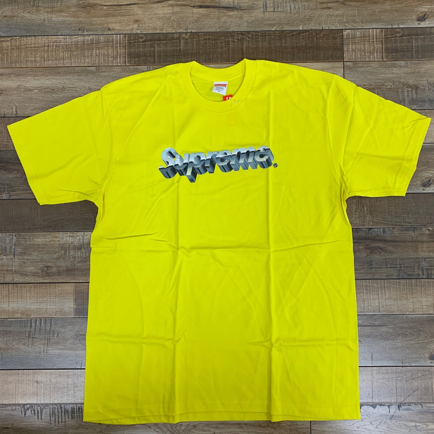 Supreme Chrome Logo Tee Yellow, brand new, displayed on wooden floor.