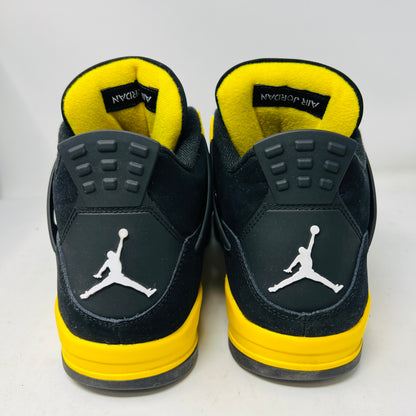 The Jordan 4 Retro Thunder (2023) features black uppers with yellow accents, a white sole, and visible air cushioning. It rests on a black and gray speckled shoebox in good condition and includes the distinctive wing design.