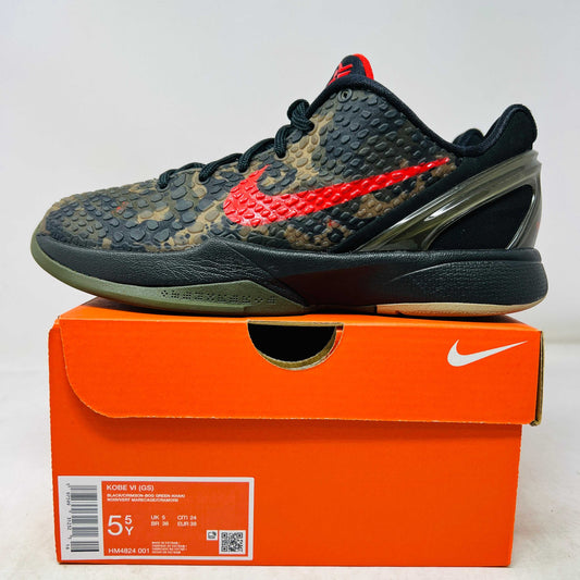 Close-up of a Nike Kobe 6 Protro Italian Camo (2024) (GS) shoe in black and dark olive with a red swoosh, resting on an orange Nike box. The 100% authentic shoe features a textured upper shown from the side, highlighting its design and striking color contrast.