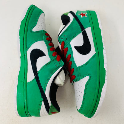 The Nike SB Dunk Low Heineken features green and white sneakers with black swoosh logos, red laces, and a red star detail on the heel against a white background.