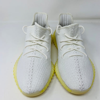 The Yeezy Boost 350 V2 Cream, by Yeezy, is displayed on a plain white background, featuring white knit material, matching laces, and yellow soles.