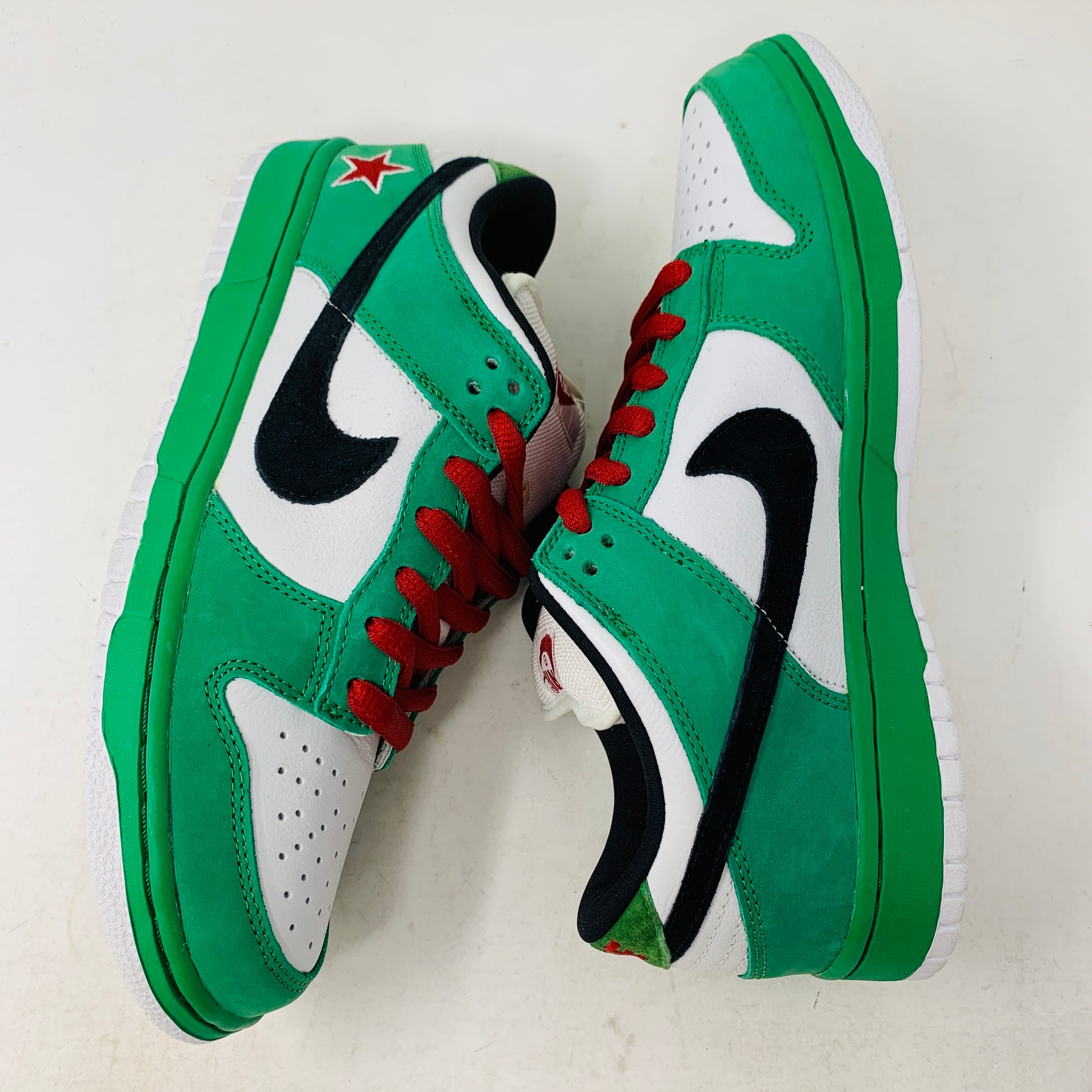 A pair of Nike SB Dunk Low Heineken sneakers with green and white panels, red laces, black swoosh logos, and a red star near the heel is displayed side by side on a white background.