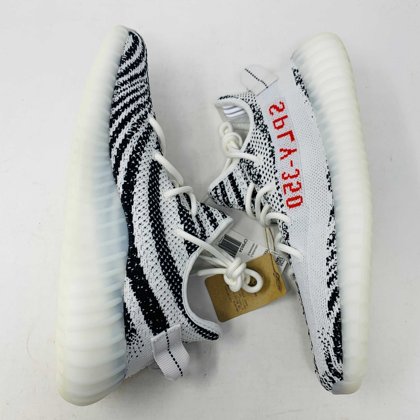 The Yeezy 350 V2 Zebra sneaker, 100% authentic, showcases SPLY-350 in bold red on a white and black design. Packaged in a box marked YZY 350 V2 MADE BY ADIDAS, it features a ribbed sole and knitted upper, effortlessly blending style and comfort.