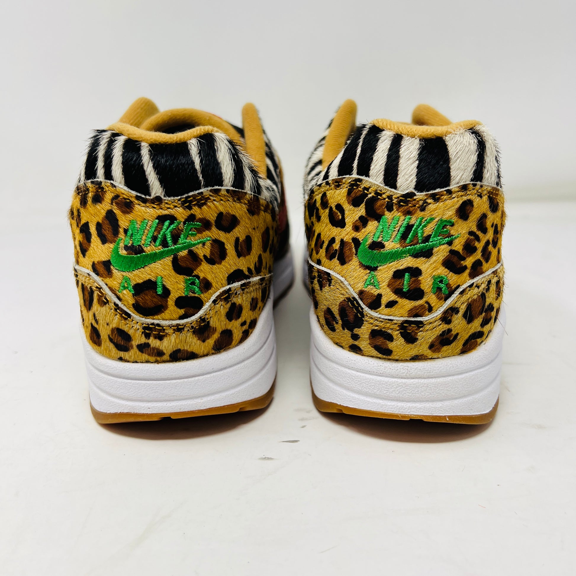 Rear view of the Nike Air Max 1 Atmos Animal Pack 2.0 sneakers featuring leopard and zebra print, a green embroidered Nike logo on the heel, and a white sole with a gum-colored bottom.