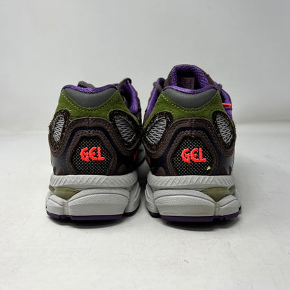 The ASICS Gel-NYC Bodega After-Hours sneakers, in brown with gray, purple, and green accents, sit on a box. A packet of extra red laces is attached. The size and details are prominently shown on the label.