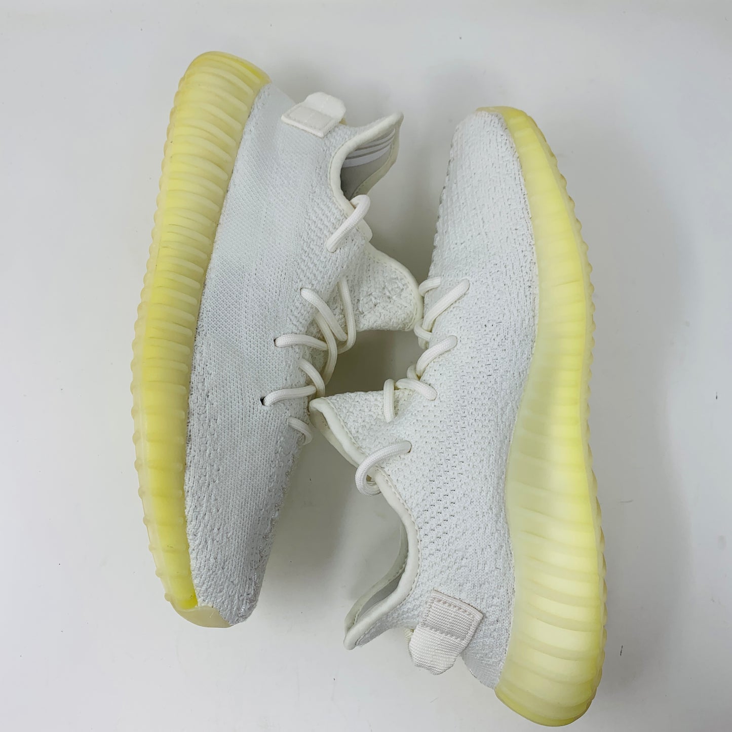 The Yeezy Boost 350 V2 Cream sneakers feature textured fabric and ribbed soles with a minimalist design. Photographed against a white background, the shoes showcase pale yellow-tinted soles.