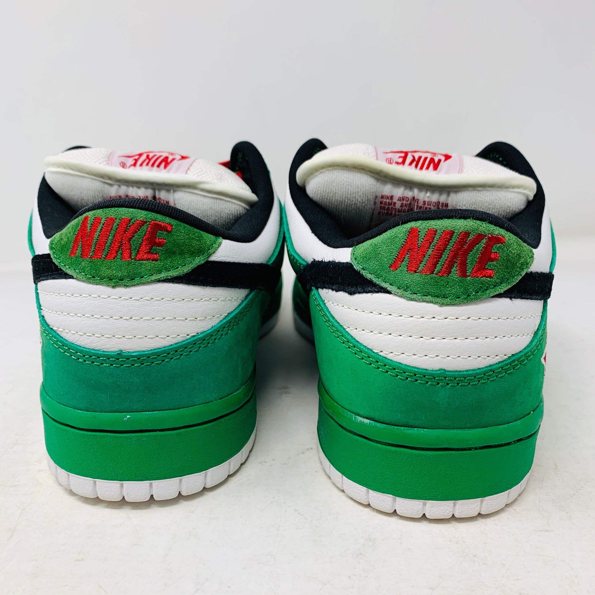 The Nike SB Dunk Low Heineken sneakers, with a green, white, and black color scheme and red branding on the heel, boast a low-top design viewed from the back.