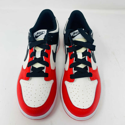 The Nike Dunk Low EMB Chicago GS, a genuine pair of red, black, and white sneakers featuring a sleek black swoosh and matching laces, elegantly sits atop a new red box adorned with bold white Nike branding.