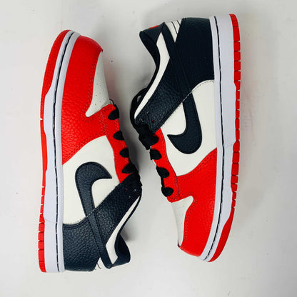 The Nike Dunk Low EMB Chicago GS, a genuine pair of red, black, and white sneakers featuring a sleek black swoosh and matching laces, elegantly sits atop a new red box adorned with bold white Nike branding.