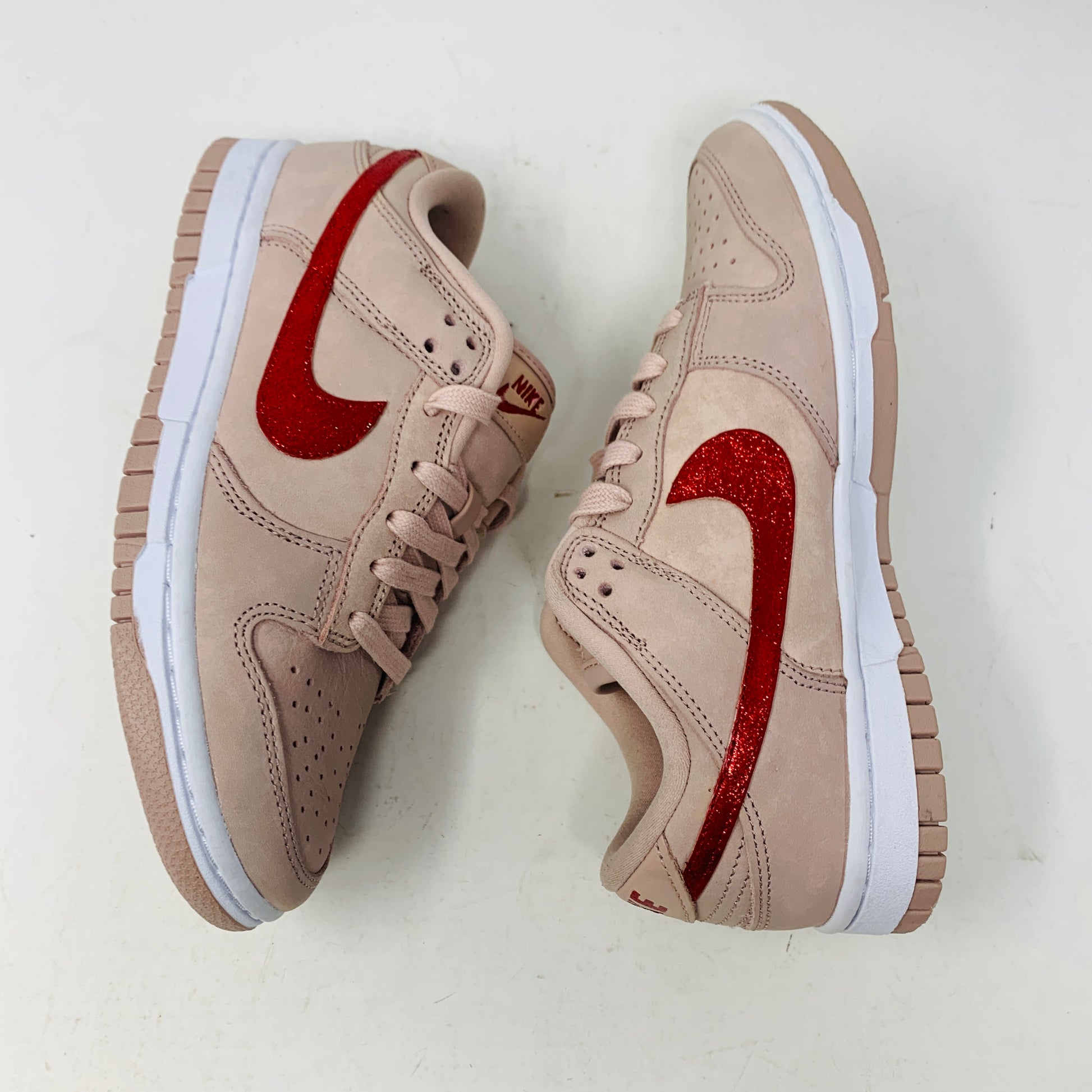 The Nike Dunk Low PRM Pink Oxford (W) Valentines Day CUSTOM features a pair of beige sneakers with red glitter swooshes, white midsoles, beige laces, and gum-colored outsoles, set side by side on a white background.